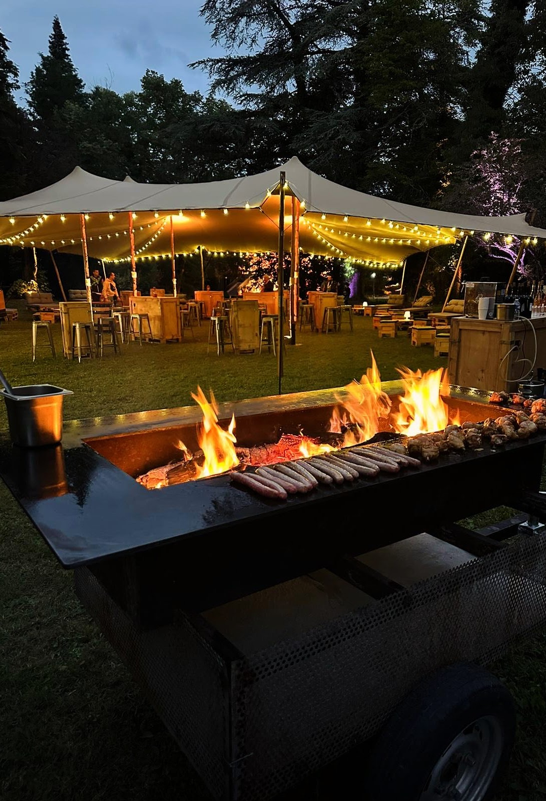 Plancha en flammes au crépuscule sous une tente illuminée lors d'une réception.
