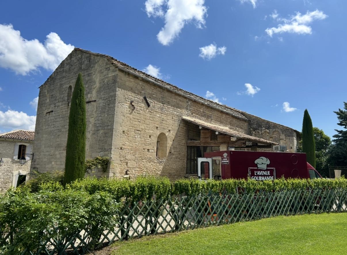 Le camion de L'avenue gourmande installé devant un mas en pierre du Luberon, cyprès et ciel d'été.