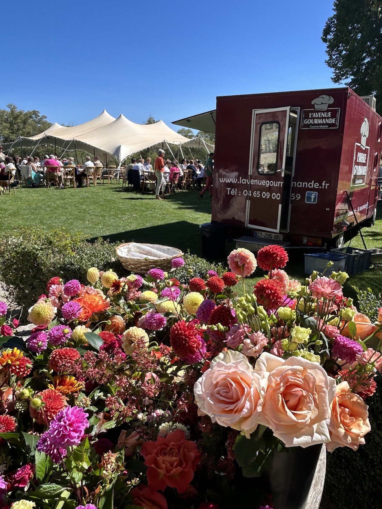 Le camion de L'avenue gourmande installé lors d'un mariage, tente de réception et massif de fleurs au premier plan.